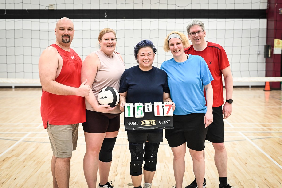 Five volleyball players posing with a ball and scoreboard.
